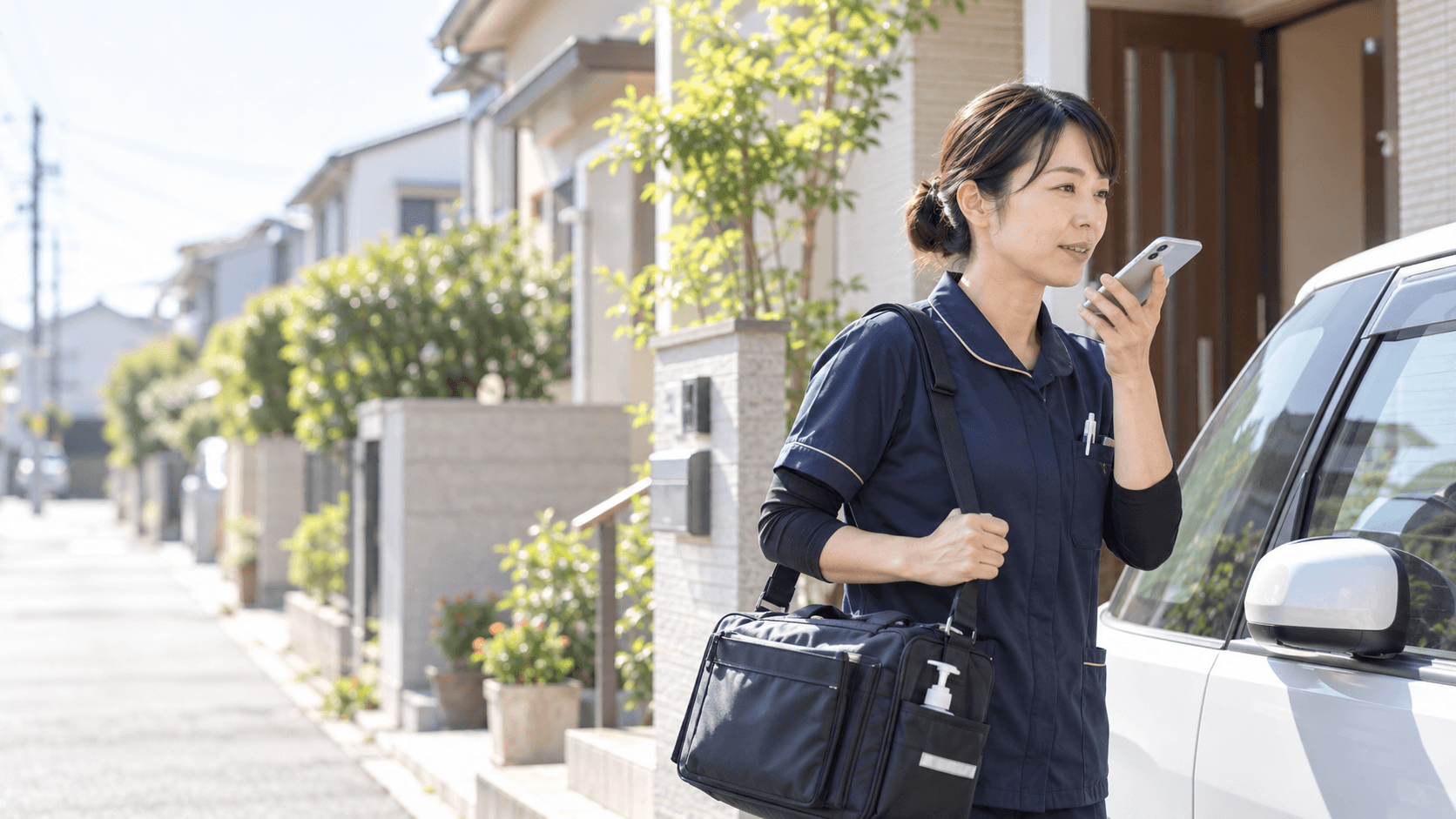 訪問先の住宅街でスマートフォンに話しかける訪問看護師のイメージ