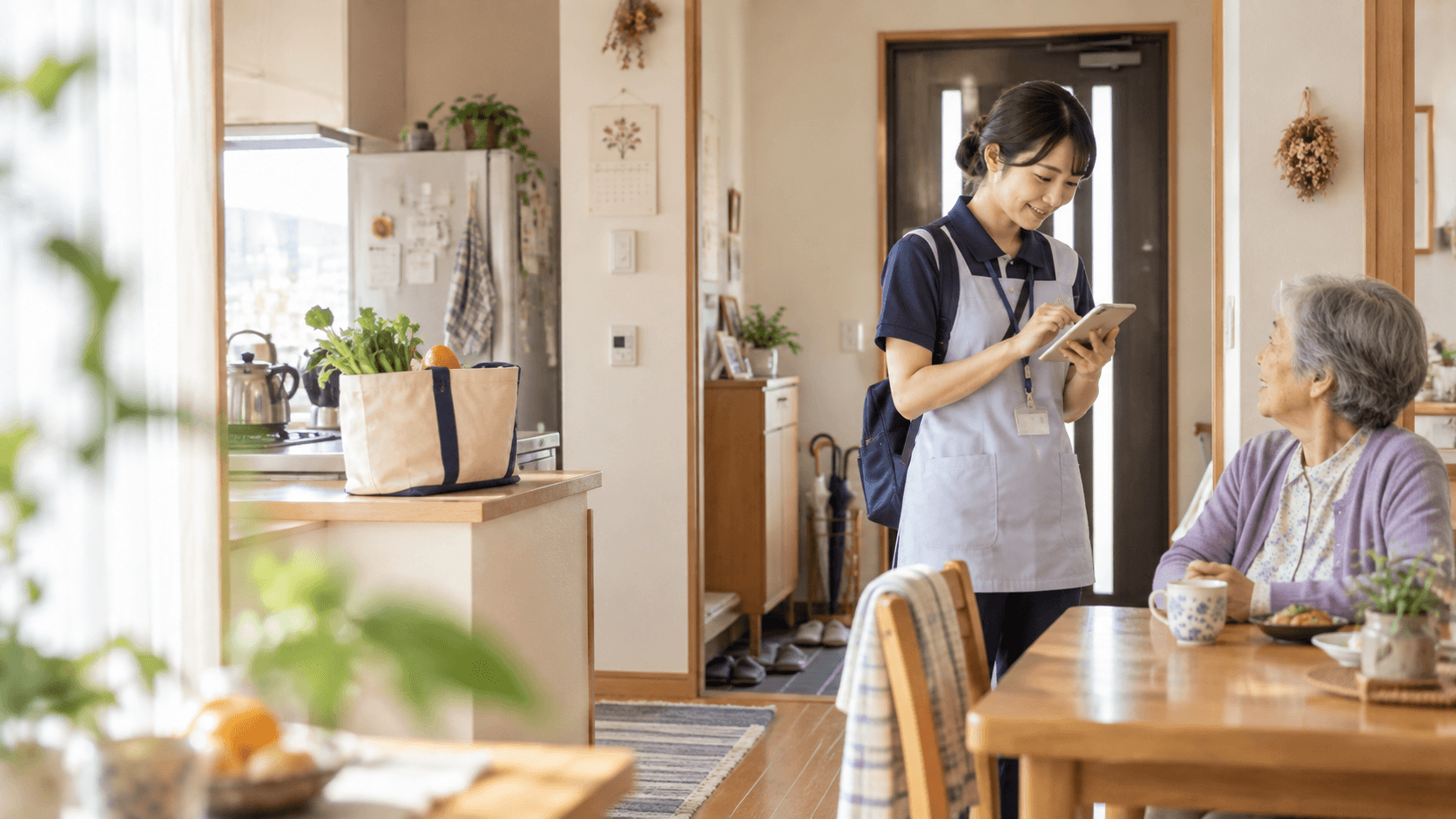 訪問先の自宅でタブレットを手に利用者と会話するホームヘルパーのイメージ